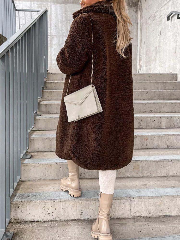 Vrouw draagt lange bruine teddy jas op buitentrap met crèmekleurige tas | Boutique Moda