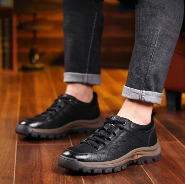 Chaussures de randonnée noires en cuir pour homme sur parquet en bois, style décontracté, semelle robuste, pantalon en jean retroussé.